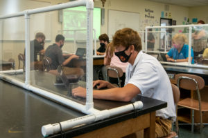 A male student during the COVID pandemic sitting in front of a plexiglass shield in the classroom | Padua Franciscan High School