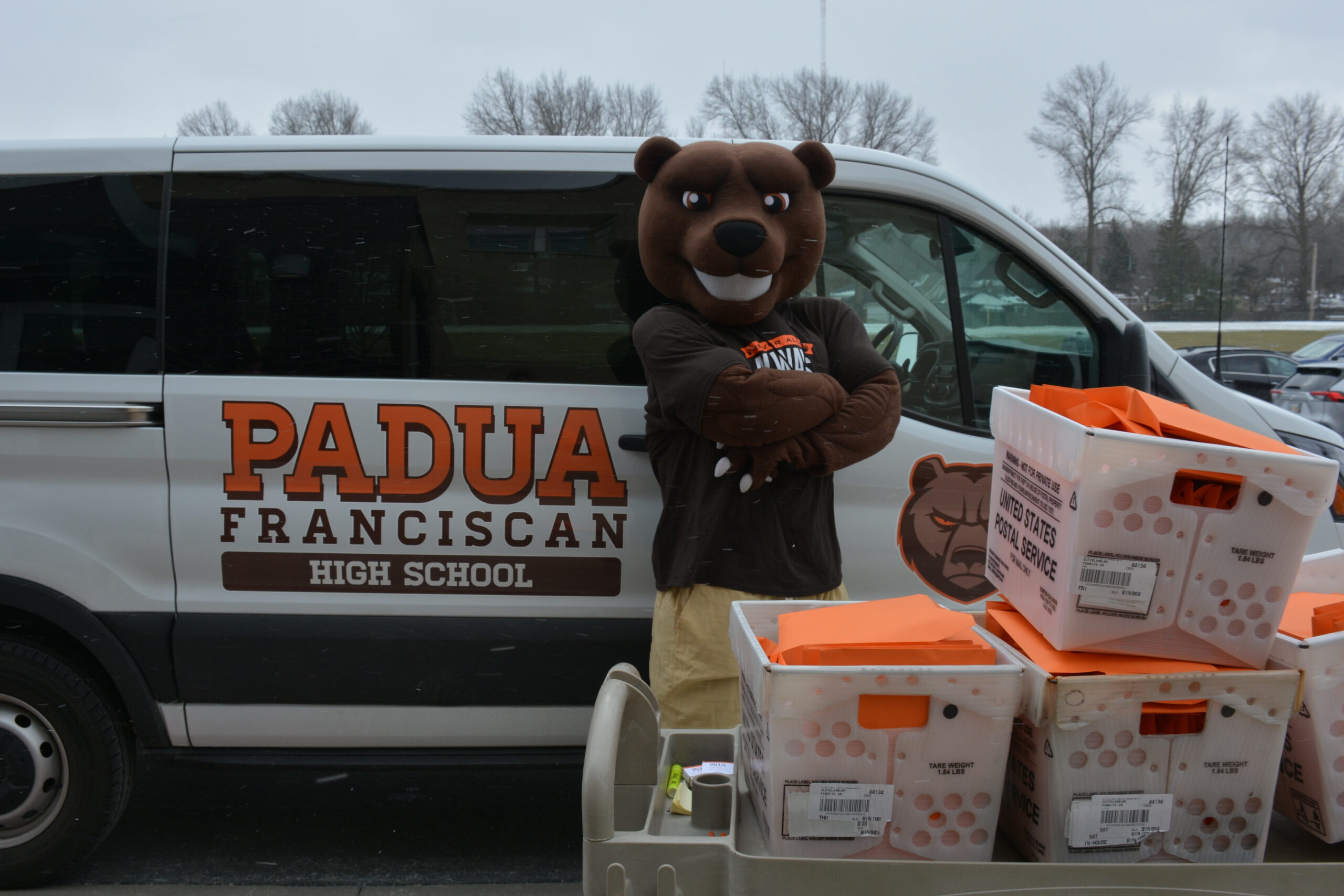 Padua Franciscan High School Mascot in front of crates of school supplies